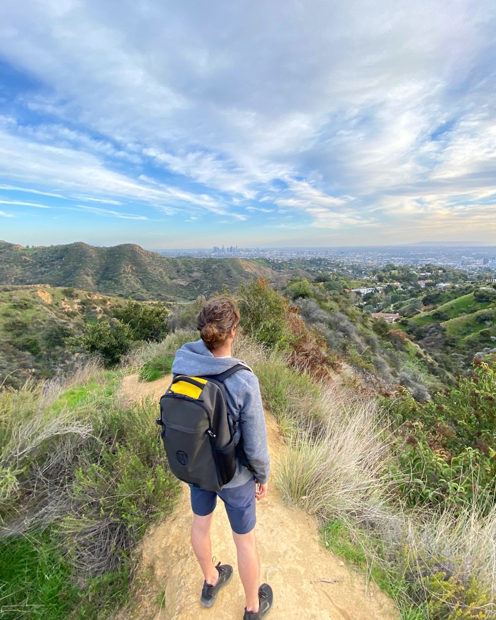 Man in shorts and hoodie wearing a backpack overlooking the Hollywood Hills in Los Angeles, California.